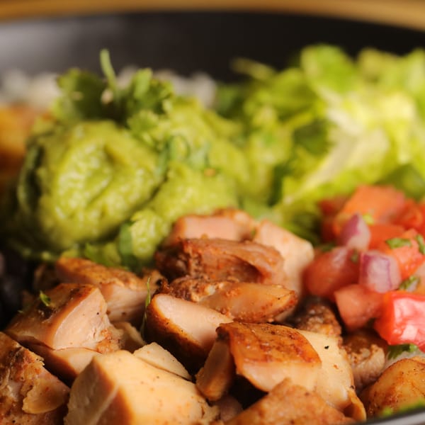 Close-up of a Bueno Burrito bowl with grilled chicken, guacamole, lettuce, and pico de gallo.