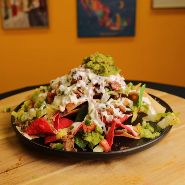A large plate of Bueno Burrito nachos with guacamole, sour cream, and red tortilla chips.