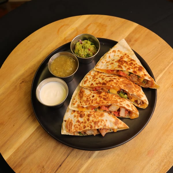 Bueno Burrito's quesadillas with guacamole, salsa verde, and sour cream on a black plate.