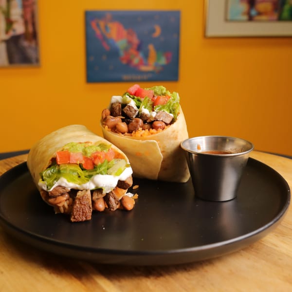 Two Bueno Burrito burritos, one cut open, filled with meat, beans, rice, lettuce, tomato, and sour cream.