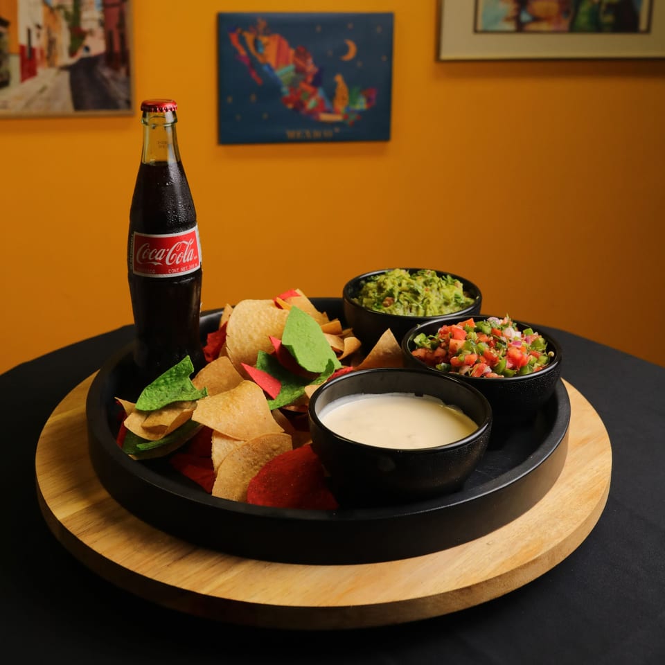 A Bueno Burrito platter with colorful tortilla chips, guacamole, pico de gallo, queso, and a Coke.
