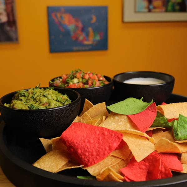 Bueno Burrito's colorful tortilla chips with guacamole, salsa, and queso dip on a black tray.
