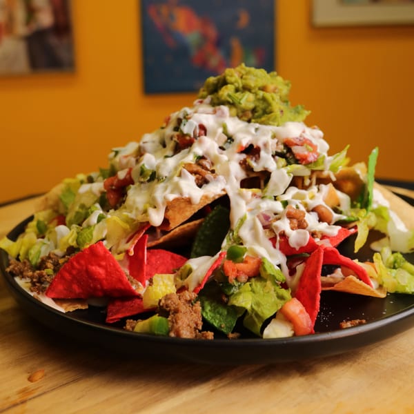 A large plate of Bueno Burrito nachos with red and yellow chips, meat, lettuce, sour cream, and guacamole.
